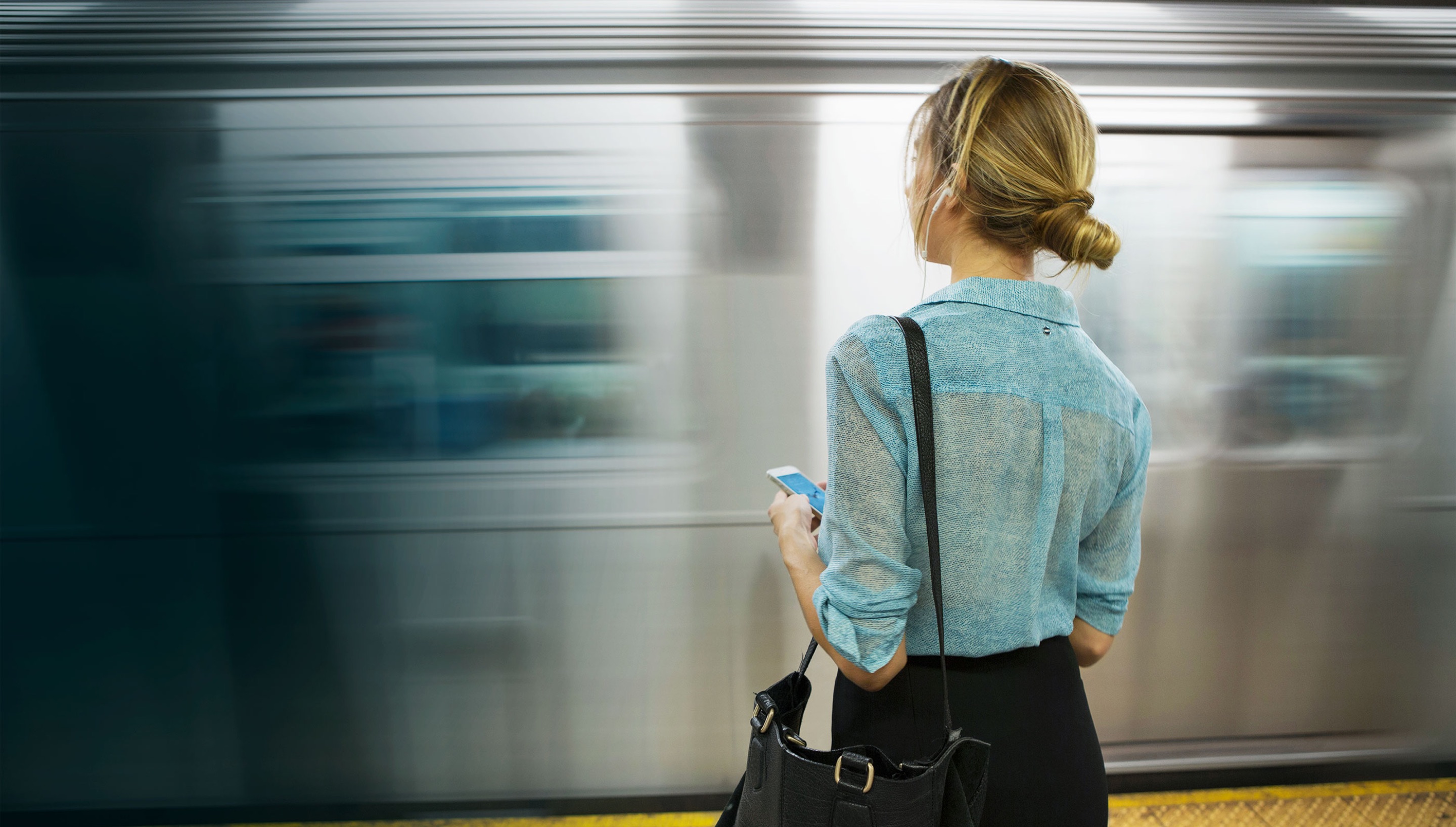 Woman with a mobile phone watching subway speed into station